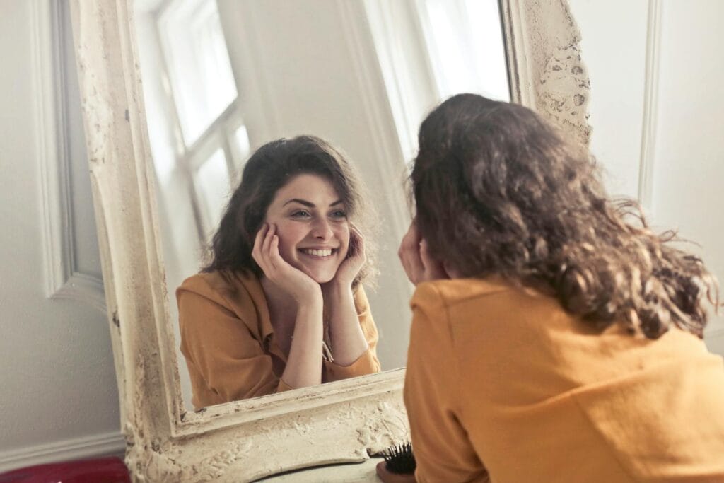 Une femme joyeuse sourit à son reflet dans un miroir de style ancien, dégageant positivité et chaleur.