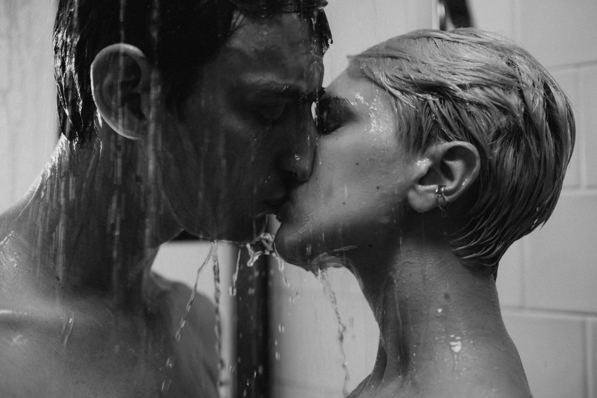 Un couple s'embrasse sous la douche, l'eau ruisselle sur leurs visages tandis que leurs yeux restent fermés, suggérant un moment d'intimité. C'est une scène qui pourrait inspirer une exploration allant au-delà d'un "Quiz sexuel pour les couples", les engageant dans leur propre test de sexualité épicé.