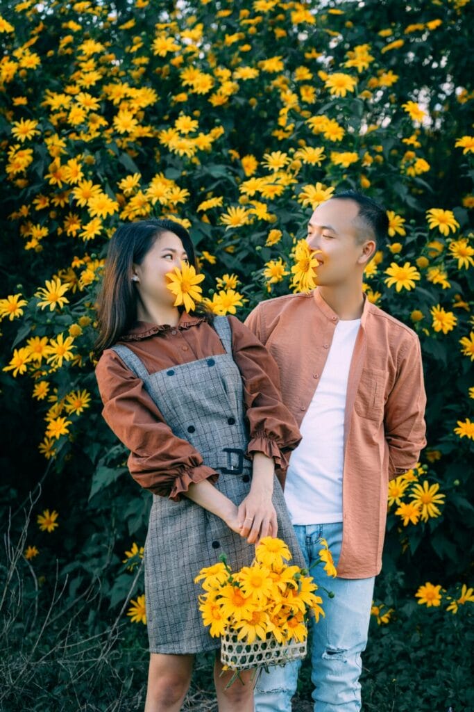 Un couple prend des photos dans un jardin botanique. Tous deux portent joyeusement des fleurs à leur bouche, comme s'ils voulaient les manger. Souriants, en tenue décontractée, ils se délectent de l'une de leurs idées de rendez-vous amusants au milieu de la beauté vibrante de la nature.