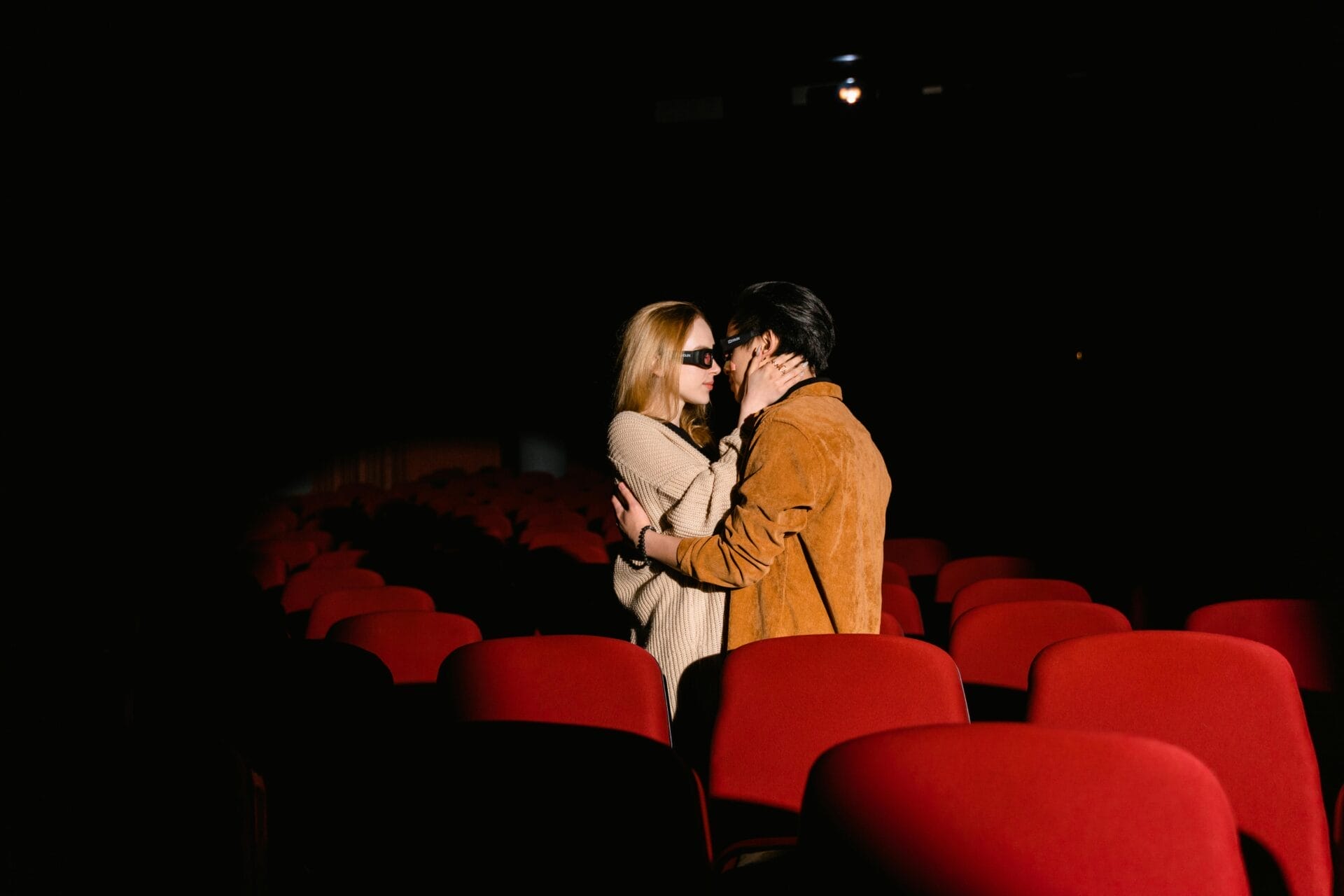 Un couple s'embrasse dans un cinéma vide, entouré de rangées de sièges rouges. Les vêtements décontractés et la lumière tamisée ajoutent un sentiment d'intimité à la scène, parfaite pour ceux qui cherchent des conseils pour sortir avec un homme Scorpion.