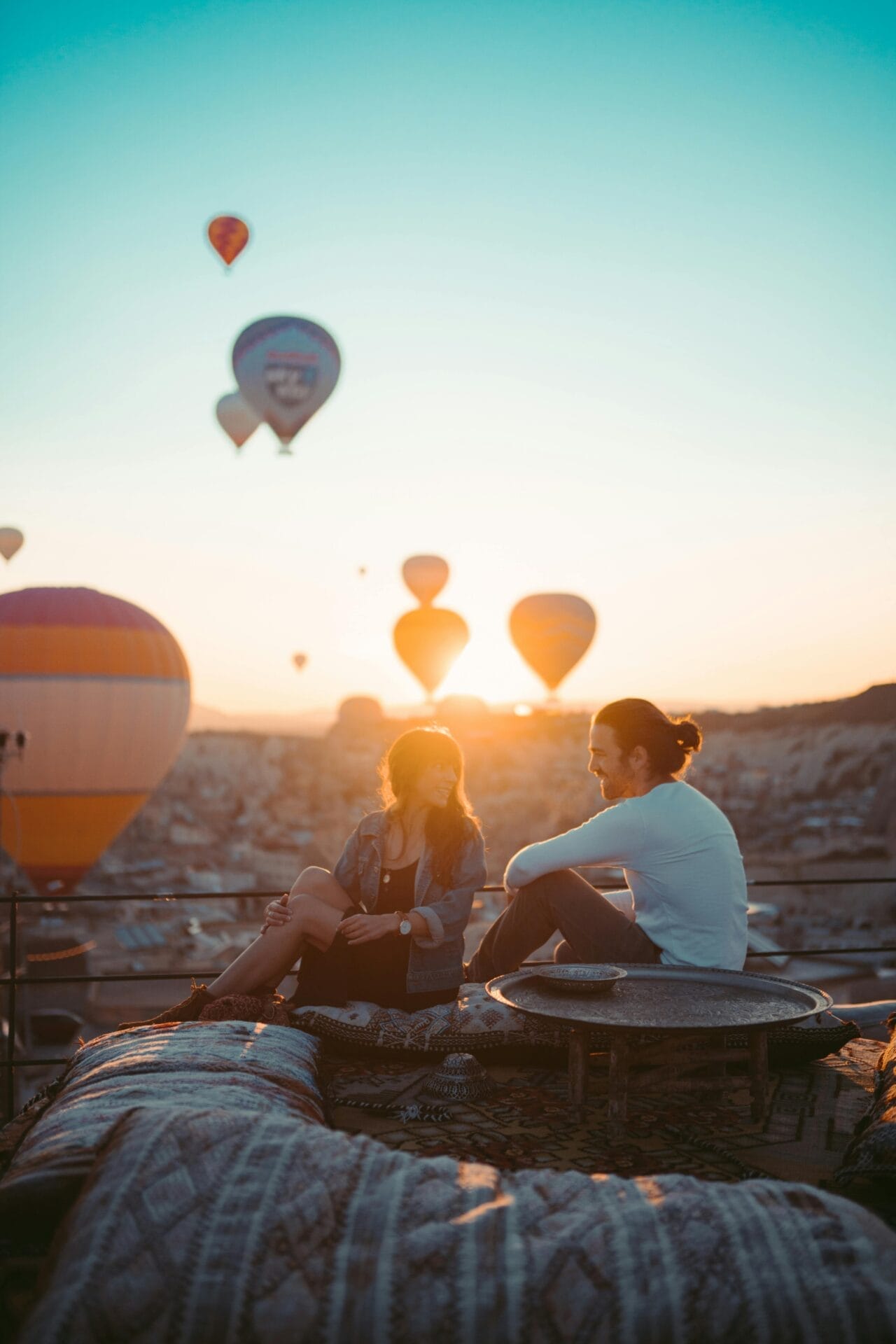 Un homme et une femme Taureau sont assis sur un toit, entourés de coussins à motifs, et regardent les montgolfières s'élever dans le ciel éclairé par le soleil levant - une scène enchanteresse de compatibilité épanouie.